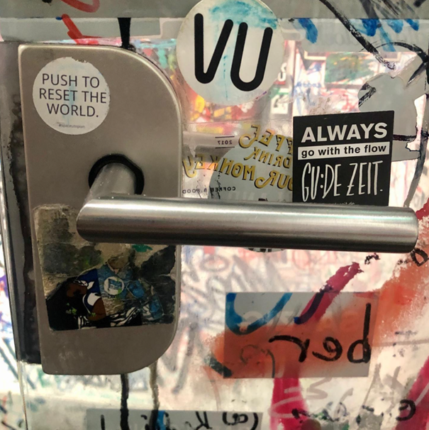 Push to reset the world, sticker art on a door handle (Berlin, DE).