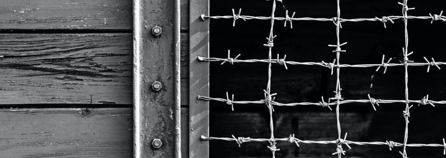 Black and white photograph of a wooden door with a barbed wire window, symbolizing confinement and restriction.